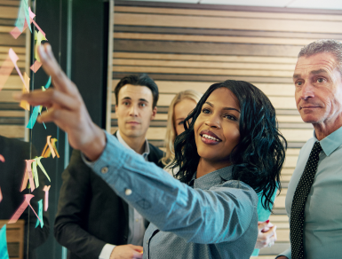 Black female pointing at board while three co workers watch