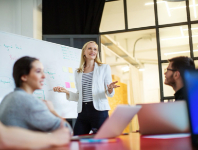 Woman presenting to an office in front of a whiteboard