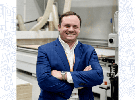 Tyler, in business attire, standing in front of medical equipment and smiling.