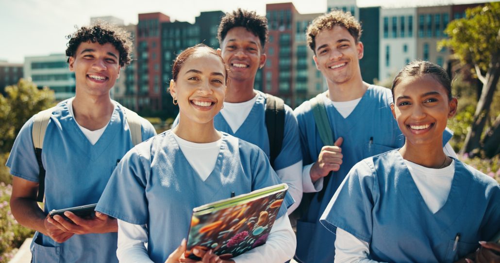 Group of 5 smiling medical students wearing scrubs