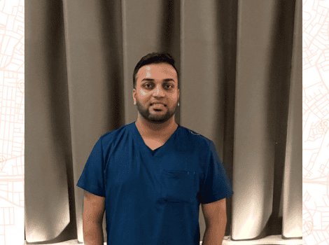 Devindra, wearing scrubs and smiling at the camera