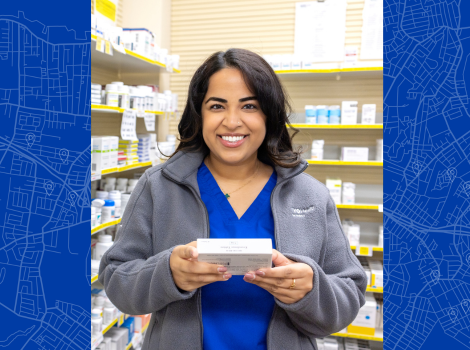 Farkhana smiling while standing in the pharmacy and holding a boxed medication