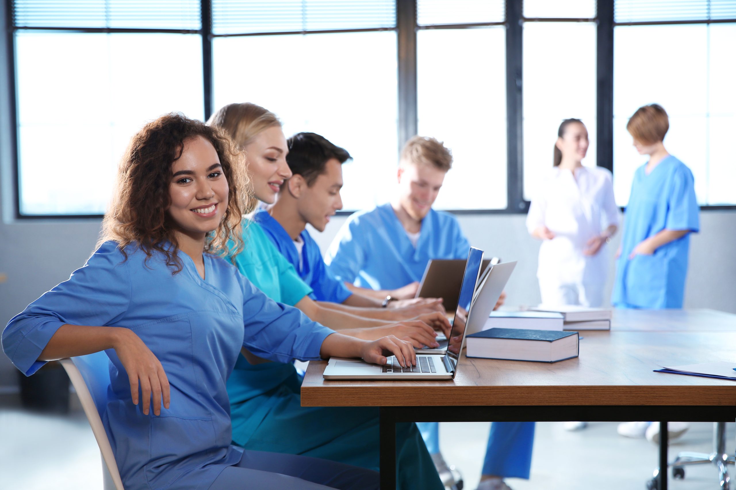 Smiling medical field students sitting at a table with laptops and books