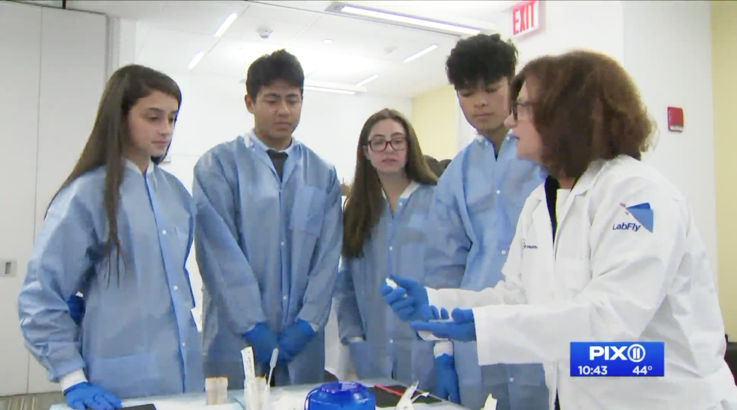 A female instructor in a white lab coat speaking with four students in blue scrub gowns