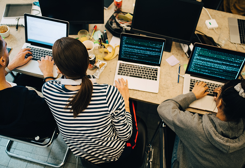 Three students sitting at a table working on laptops together